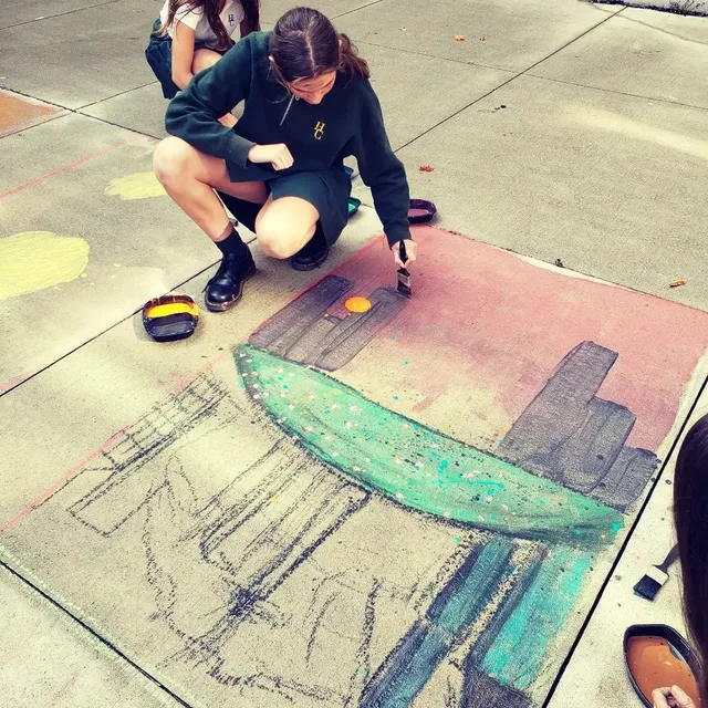 A volunteer painting a colourful mural on the pavement